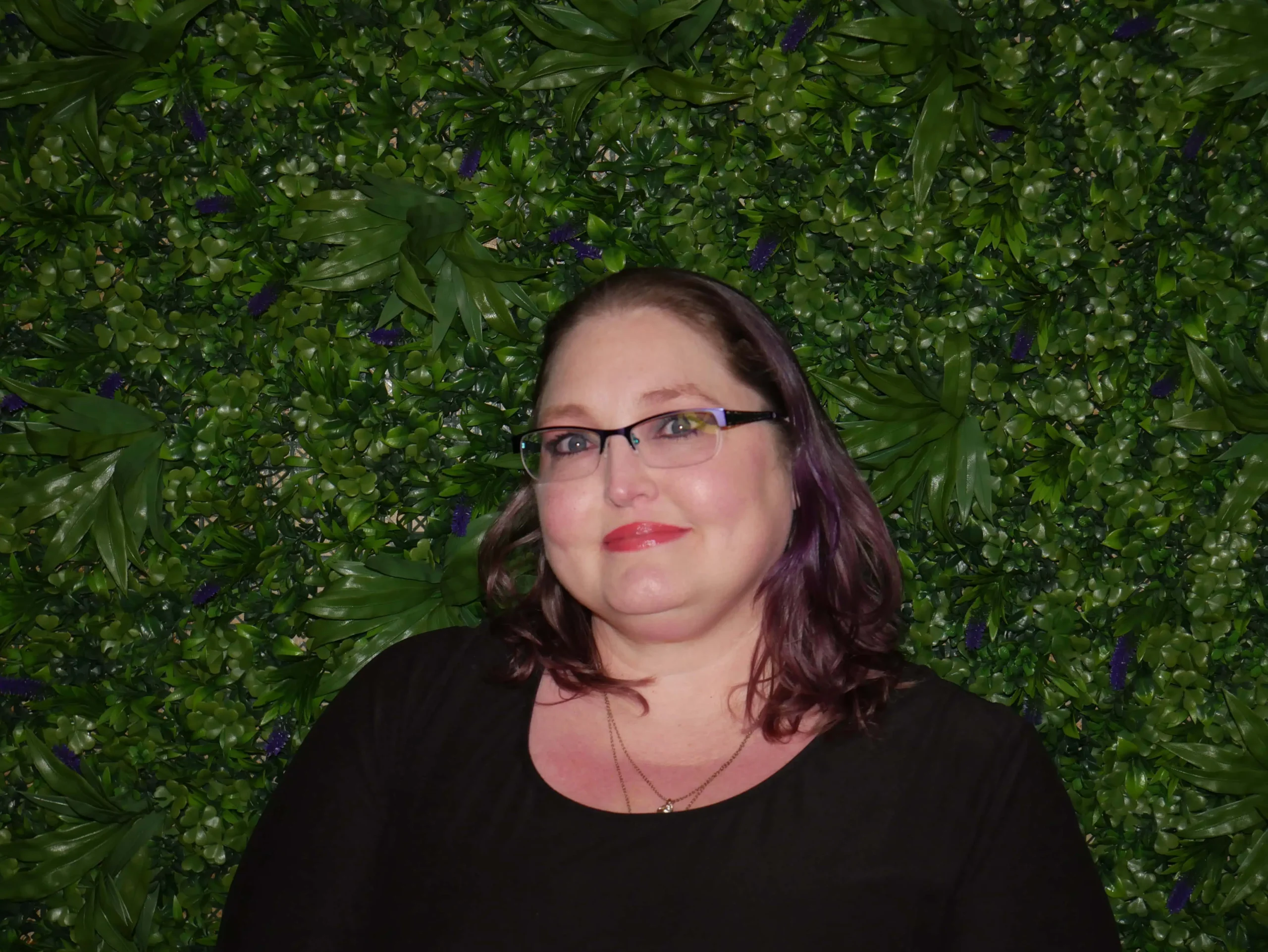 a woman in glasses smiling in front of a green wall