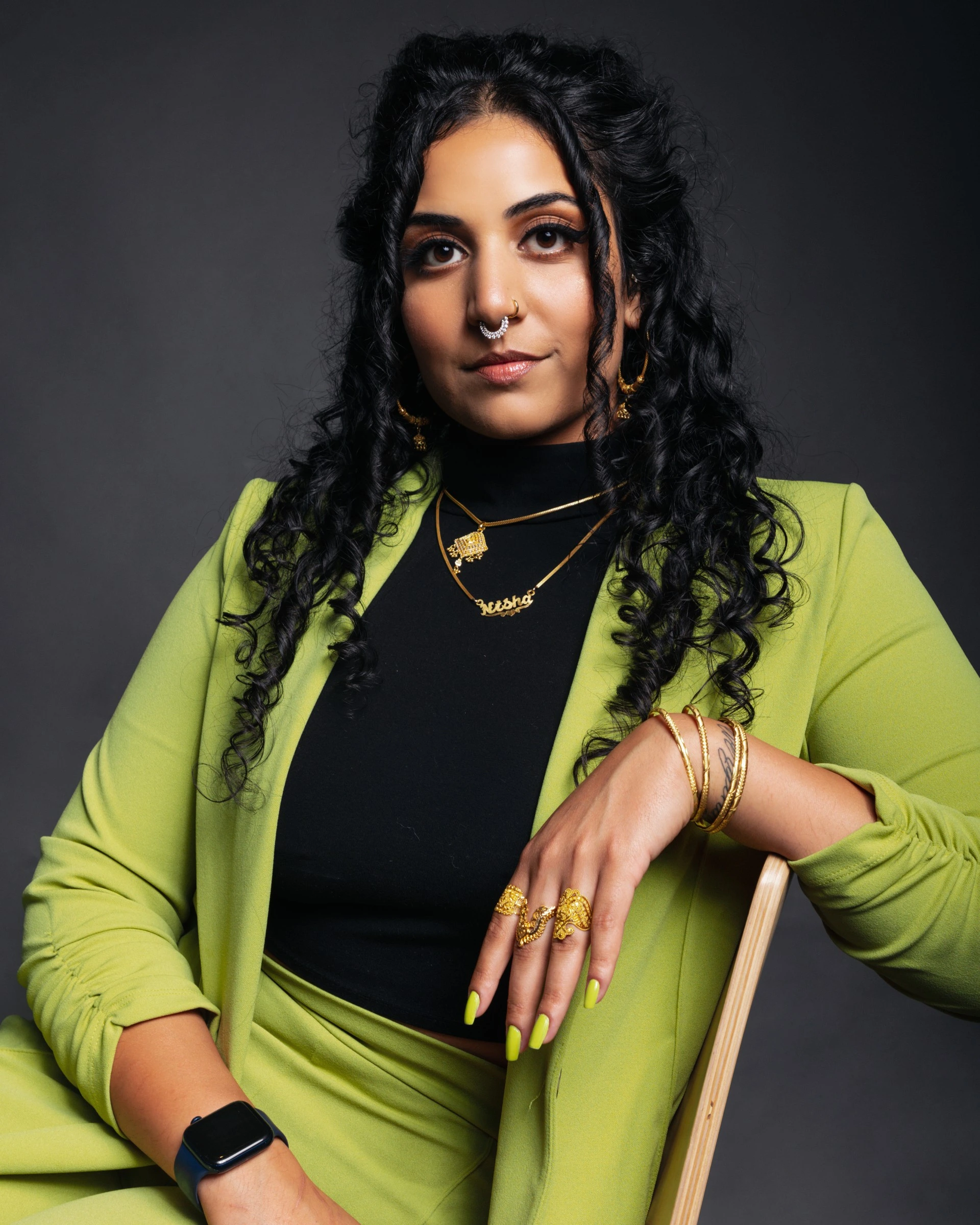 a woman with black curly hair wearing a green suit and gold jewelry