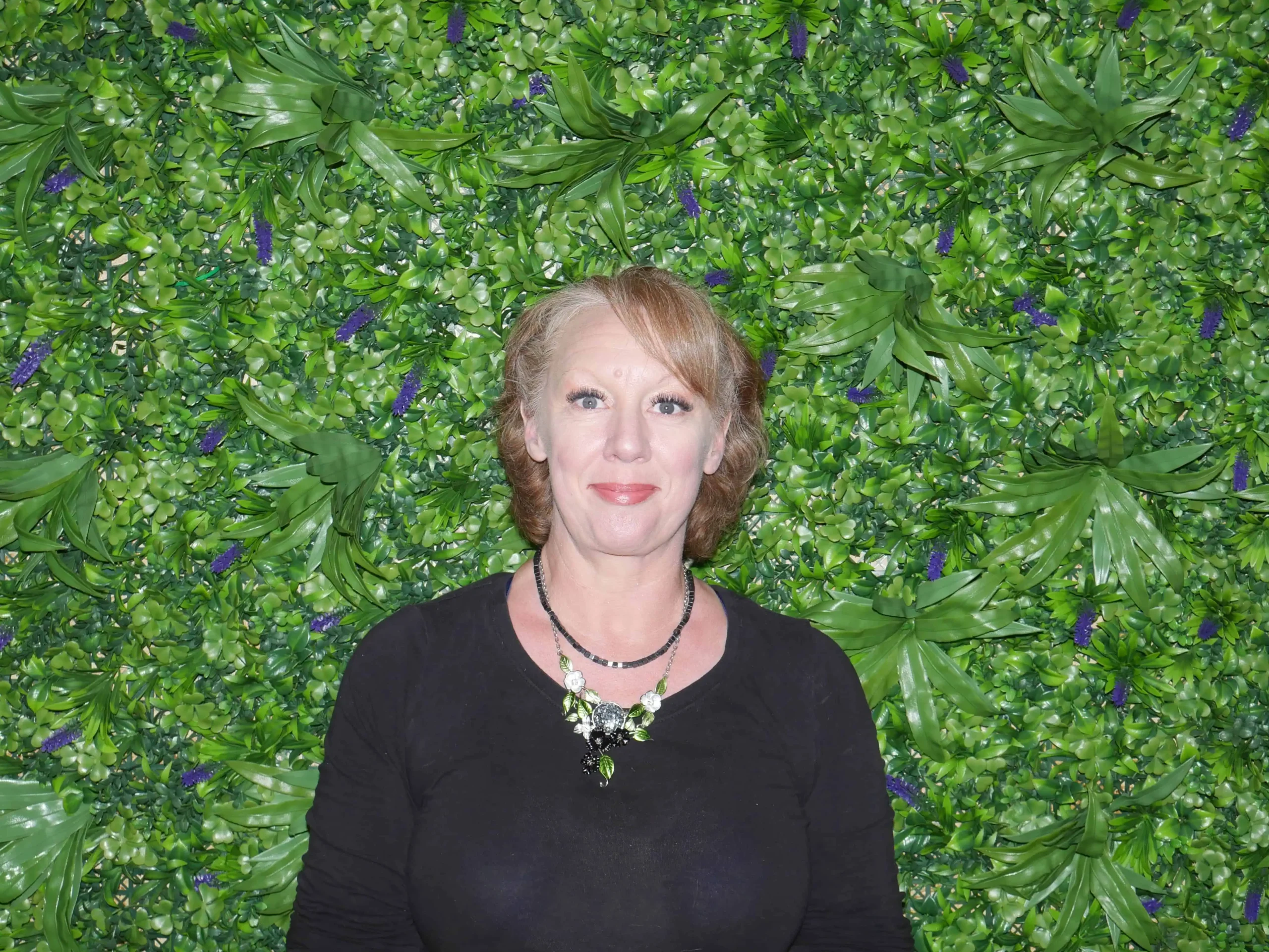 a woman standing in front of a wall of leaves